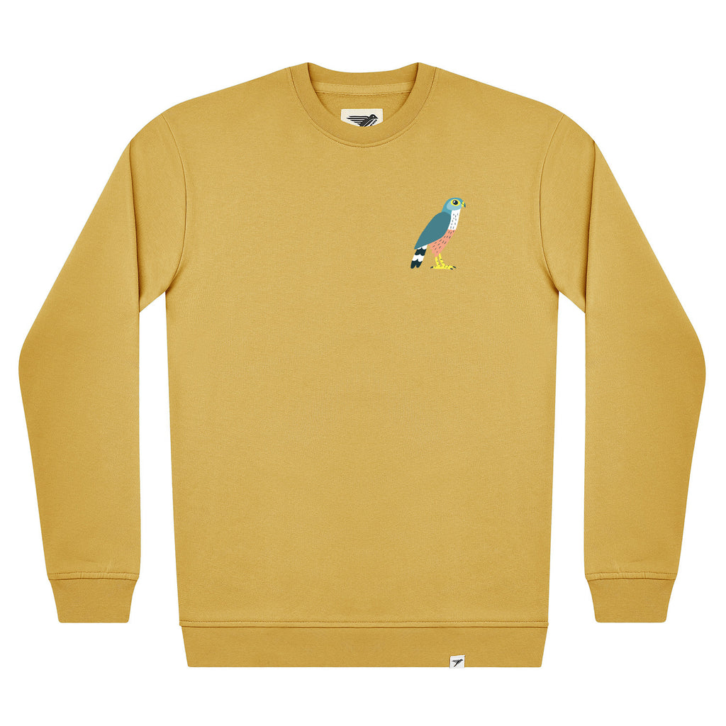 A mustard yellow crewneck sweatshirt featuring a small colorful embroidered merlin bird on the left chest, displayed on a clean white background.